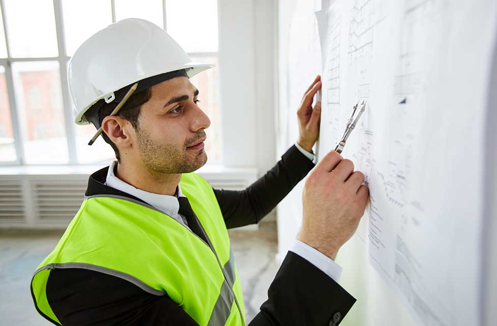 Ein Bau-Gutachter kontrolliert den Bauplan an der Zimmerwand