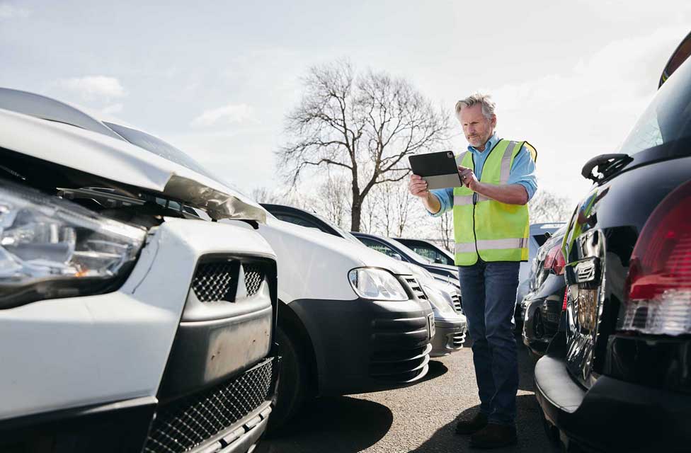 Schadensgutachter mit Tablet prüft einen Frontschaden bei einem weisen Auto.