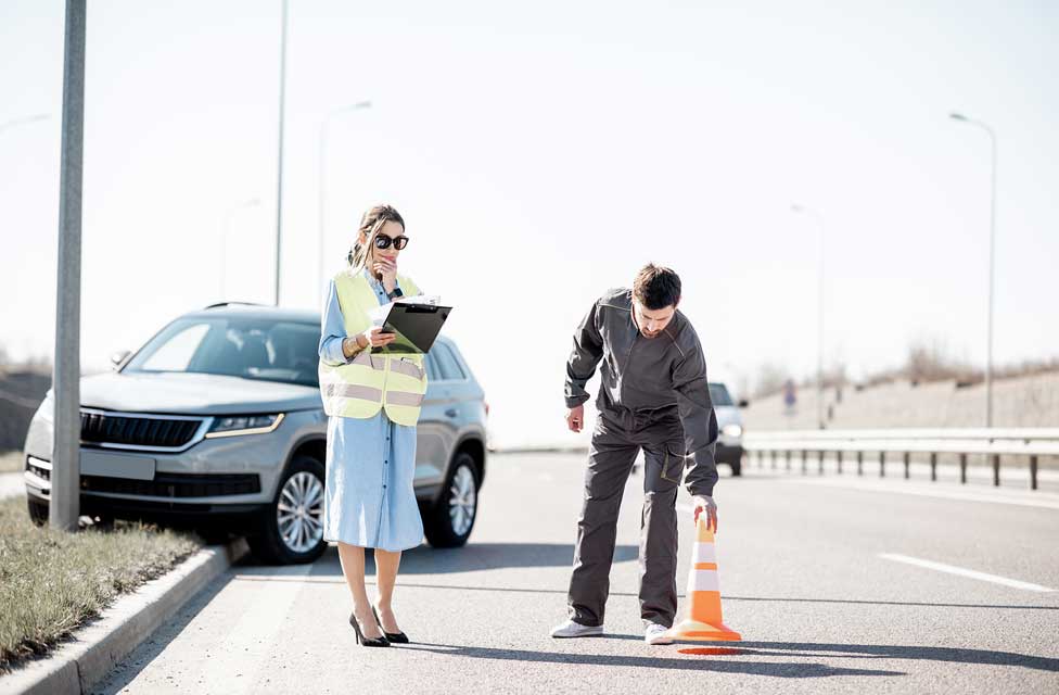 Weiblicher Kfz Sachverständige mit Helfer rekonstruieren einen Unfall auf der Straße das beschädigte Fahrzeug steht an der Laterne